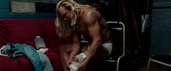 Movie still from “The Wrestler” (2008), directed by Darren Aronofsky – A man sitting on a chair with a bandage on his knee; Medium shot, Low angle