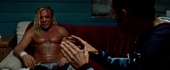 Movie still from “The Wrestler” (2008), directed by Darren Aronofsky – A man sitting on a red couch next to another man clapping; Medium shot, Over the shoulder angle