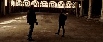 Movie still from “The Wrestler” (2008), directed by Darren Aronofsky – Two people standing in an empty room with a stained - glass window in the background; Wide shot, Low angle