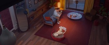 Movie still from “DC League of Super-Pets” (2022), directed by Jared Stern – A man sitting on a couch in a living room with a dog laying on the floor; Wide shot, High angle