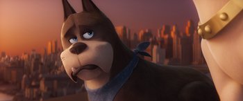 Movie still from “DC League of Super-Pets” (2022), directed by Jared Stern – A dog with a bandana around its neck is standing in front of a city skyline at sunset; Close Up shot, Over the shoulder angle
