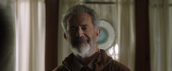 Movie still from “Dangerous” (2021), directed by David Hackl – An older man with a gray beard wearing a brown jacket; Close Up shot, Over the shoulder angle