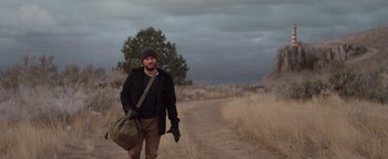 Movie still from “Dangerous” (2021), directed by David Hackl – A man walking down a dirt road holding a bag; Wide shot, Low angle