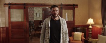 Movie still from “Dangerous” (2021), directed by David Hackl – A man standing in a living room wearing a sweater; Medium shot, Over the shoulder angle
