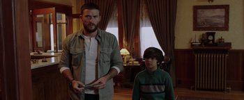 Movie still from “Dangerous” (2021), directed by David Hackl – A man standing next to a young boy holding a nintendo wii game controller; Medium shot, Low angle