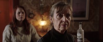 Movie still from “Dangerous” (2021), directed by David Hackl – An older woman looking at the camera in a dark room; Close Up shot, Over the shoulder angle