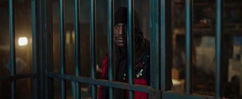 Movie still from “Dangerous” (2021), directed by David Hackl – A man in a red and black jacket behind a metal fence; Medium shot, High angle