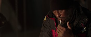 Movie still from “Dangerous” (2021), directed by David Hackl – A man with a cigarette in his mouth and wearing a hat; Close Up shot, High angle