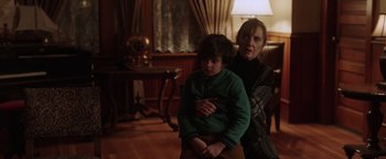 Movie still from “Dangerous” (2021), directed by David Hackl – An older woman and a young boy sitting in a living room; Medium shot, Over the shoulder angle