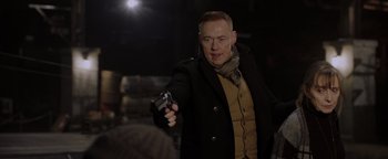 Movie still from “Dangerous” (2021), directed by David Hackl – A man holding a gun while standing in a dark room; Medium shot, Over the shoulder angle