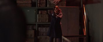 Movie still from “Dangerous” (2021), directed by David Hackl – A woman holding a gun in a room filled with boxes; Medium shot, Over the shoulder angle