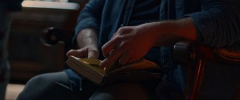 Movie still from “Dangerous Game: The Legacy Murders” (2022), directed by Sean McNamara – A person is reading a book in a dark room; Extreme Close Up shot, High angle