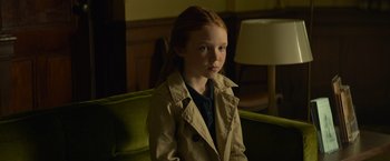 Movie still from “Dark Phoenix” (2019), directed by Simon Kinberg – A young girl sitting on a green chair wearing a trench coat; Medium shot, High angle