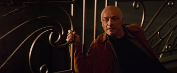 Movie still from “Dark Phoenix” (2019), directed by Simon Kinberg – A bald man holding a metal bar behind a fence; Medium shot, Low angle