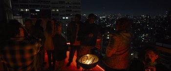 Movie still from “To Catch a Killer” (2023), directed by Damián Szifron – A group of people standing around an open fire pit; Extreme Wide shot, High angle