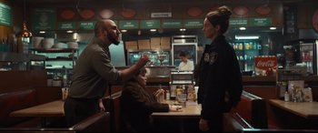 Movie still from “To Catch a Killer” (2023), directed by Damián Szifron – A group of people standing around a table in a room; Medium shot, Over the shoulder angle