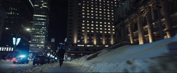 Movie still from “To Catch a Killer” (2023), directed by Damián Szifron – A person riding a bike on a snowy path in front of a tall building; Extreme Wide shot, Low angle