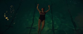 Movie still from “To Catch a Killer” (2023), directed by Damián Szifron – A woman in a black bathing suit swimming in a pool; Wide shot, Overhead angle