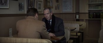 Movie still from “To Catch a Killer” (2023), directed by Damián Szifron – A man sitting at a table talking to another man; Medium shot, Over the shoulder angle