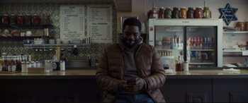 Movie still from “To Catch a Killer” (2023), directed by Damián Szifron – A man sitting in front of a counter looking at his cell phone; Medium shot, Over the shoulder angle
