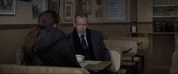 Movie still from “To Catch a Killer” (2023), directed by Damián Szifron – A man sitting at a table with a cup of coffee in front of him; Medium shot, Over the shoulder angle