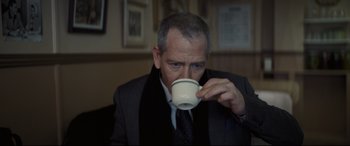 Movie still from “To Catch a Killer” (2023), directed by Damián Szifron – A man drinking a cup of coffee from a white cup; Close Up shot, Over the shoulder angle