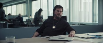 Movie still from “To Catch a Killer” (2023), directed by Damián Szifron – A man sitting at a table in an office setting; Medium shot, Low angle