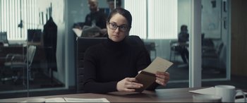 Movie still from “To Catch a Killer” (2023), directed by Damián Szifron – A woman sitting at a table holding a book; Medium shot, Over the shoulder angle