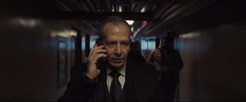Movie still from “To Catch a Killer” (2023), directed by Damián Szifron – A man wearing a suit and tie talking on a cell phone; Medium shot, Over the shoulder angle