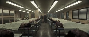 Movie still from “To Catch a Killer” (2023), directed by Damián Szifron – A group of people sitting on top of tables in a room; Extreme Wide shot, High angle