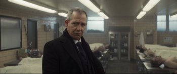 Movie still from “To Catch a Killer” (2023), directed by Damián Szifron – A man in a suit and tie standing in a room; Close Up shot, Over the shoulder angle