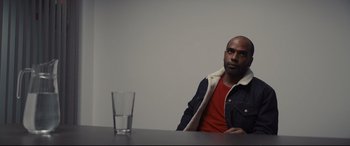 Movie still from “To Catch a Killer” (2023), directed by Damián Szifron – A man sitting in front of a glass of water; Medium shot, Over the shoulder angle