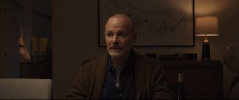 Movie still from “To Catch a Killer” (2023), directed by Damián Szifron – A man with a shaved head is sitting in a room; Close Up shot, Over the shoulder angle