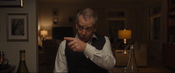 Movie still from “To Catch a Killer” (2023), directed by Damián Szifron – An older man pointing to the side of his face; Medium shot, Over the shoulder angle