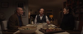 Movie still from “To Catch a Killer” (2023), directed by Damián Szifron – A man sitting at a table with a plate of food in front of him; Medium shot, Over the shoulder angle