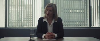 Movie still from “To Catch a Killer” (2023), directed by Damián Szifron – A woman sitting at a table in front of a glass of water; Medium shot, Over the shoulder angle