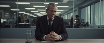 Movie still from “To Catch a Killer” (2023), directed by Damián Szifron – A man sitting at a table in a suit and tie; Medium shot, Over the shoulder angle