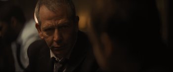 Movie still from “To Catch a Killer” (2023), directed by Damián Szifron – An older man wearing a suit and tie looking at the camera; Close Up shot, Over the shoulder angle