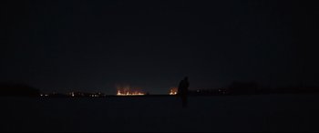 Movie still from “To Catch a Killer” (2023), directed by Damián Szifron – A man standing on a beach at night with lights in the background; Extreme Wide shot, Low angle