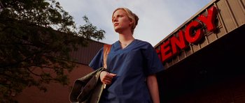 Movie still from “Dawn of the Dead” (2004), directed by Zack Snyder – A woman in scrubs holding a bag in front of a building; Medium shot, Low angle