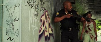 Movie still from “Dawn of the Dead” (2004), directed by Zack Snyder – A man in a police uniform standing in front of a wall; Medium shot, Low angle