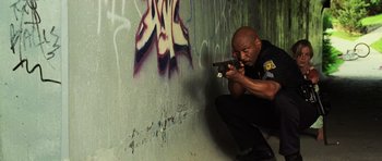 Movie still from “Dawn of the Dead” (2004), directed by Zack Snyder – A police officer is aiming a gun at a graffiti wall; Medium shot, Low angle
