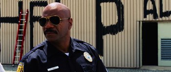 Movie still from “Dawn of the Dead” (2004), directed by Zack Snyder – A police officer wearing sunglasses in front of a building; Close Up shot, Low angle