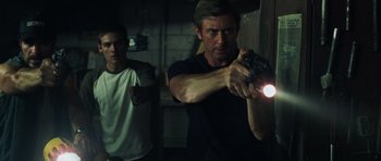 Movie still from “Dawn of the Dead” (2004), directed by Zack Snyder – A man holding a gun in a room with another man standing next to him; Medium shot, Low angle