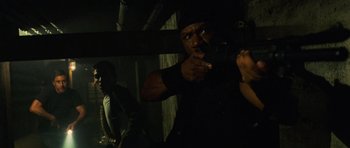 Movie still from “Dawn of the Dead” (2004), directed by Zack Snyder – A man pointing a gun at the camera in the dark; Medium shot, Over the shoulder angle