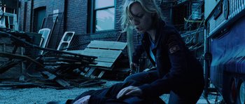 Movie still from “Dawn of the Dead” (2004), directed by Zack Snyder – A woman sitting on the ground in front of a brick building; Medium shot, Over the shoulder angle