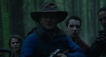 Movie still from “Dawn of the Planet of the Apes” (2014), directed by Matt Reeves – A man in a hat and jacket holding a gun; Medium shot, Over the shoulder angle
