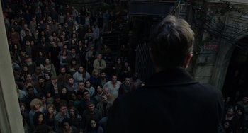 Movie still from “Dawn of the Planet of the Apes” (2014), directed by Matt Reeves – A crowd of people sitting in front of a man in a black jacket; Wide shot, High angle