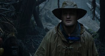 Movie still from “Dawn of the Planet of the Apes” (2014), directed by Matt Reeves – A man wearing a rain coat and hat in the woods; Close Up shot, Low angle