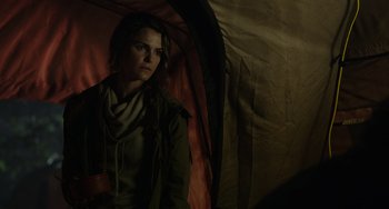 Movie still from “Dawn of the Planet of the Apes” (2014), directed by Matt Reeves – A woman standing inside of an open tent looking at the camera; Medium shot, Over the shoulder angle